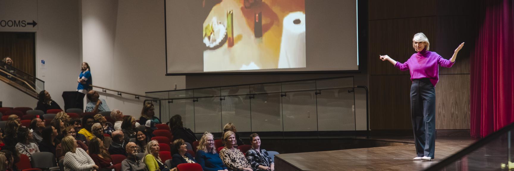Woman standing on stage in front of audience with screen behind her