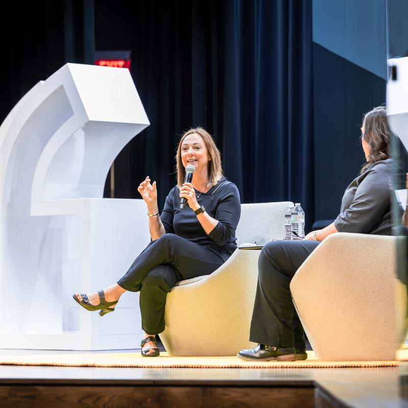 Susan Cain sits on the stage holding a microphone with large white quote marks behind her